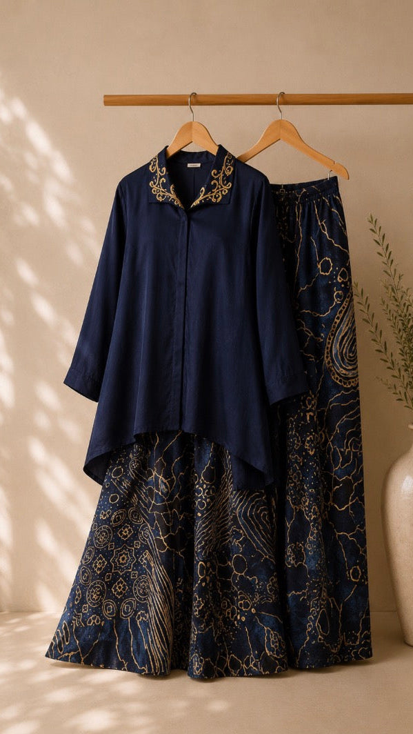 Navy blue shirt and long patterned skirt set on hangers against a beige wall with a vase and plant.